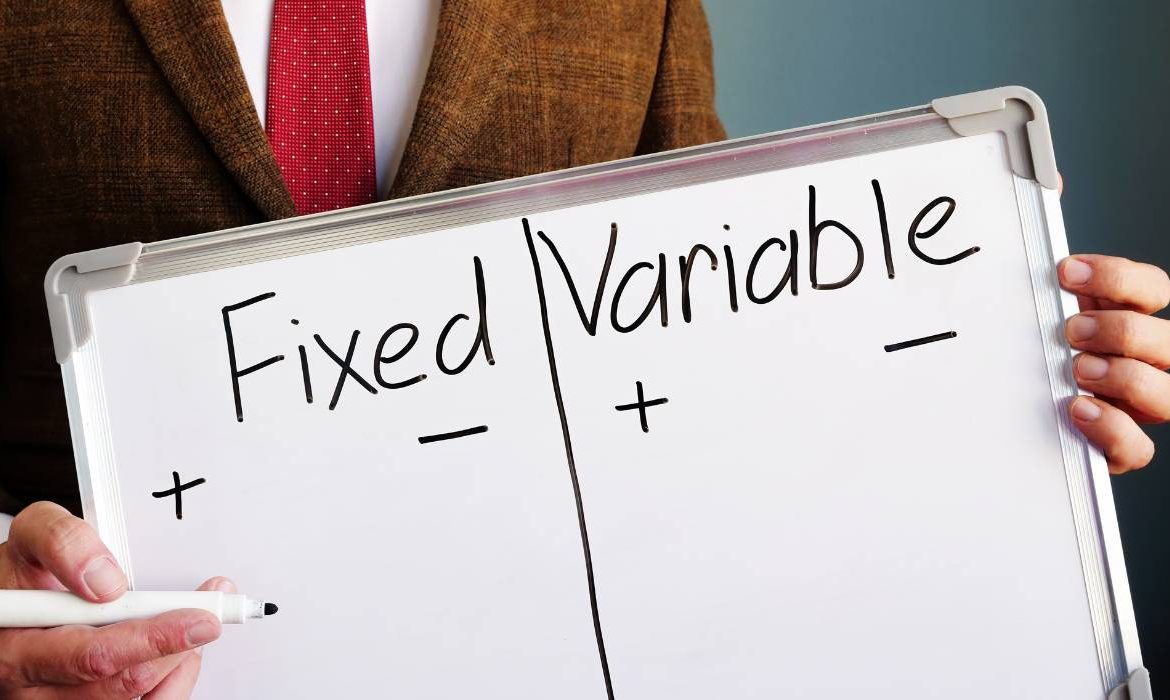 A person in a suit holding up a white board with the words fixed variable written on it