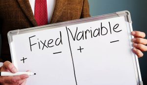 A person in a suit holding up a white board with the words fixed variable written on it